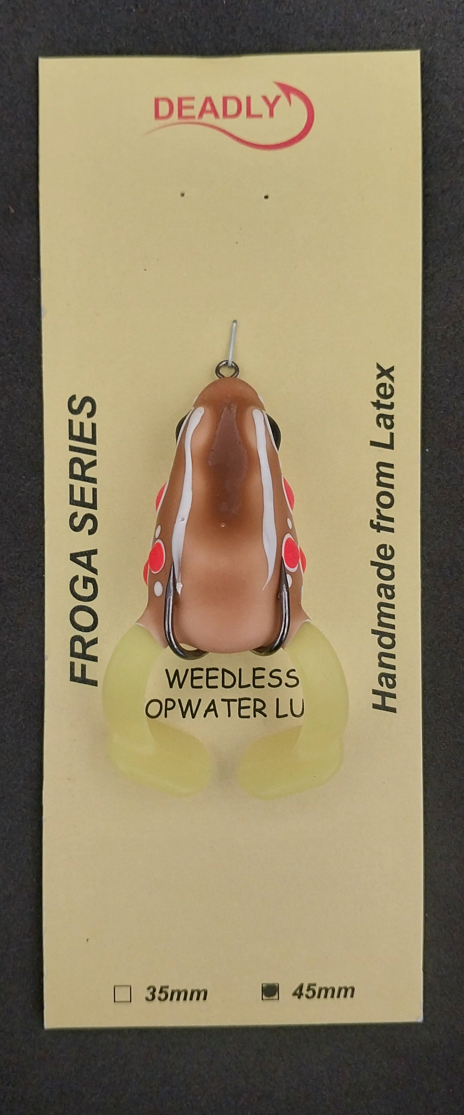 Frog-shaped fishing lure on a card with branding and product details against a dark background